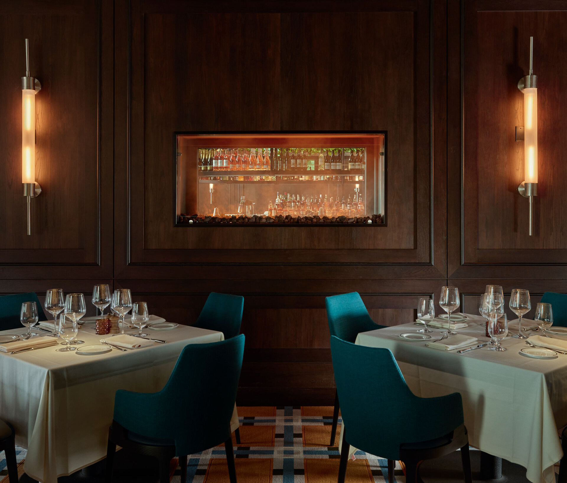 Wood-paneled wall with brass sconces and a recessed illuminated bar opening